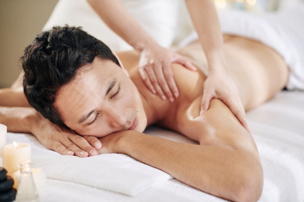 Homem recebendo massagem relaxante nas costas em ambiente de spa com velas