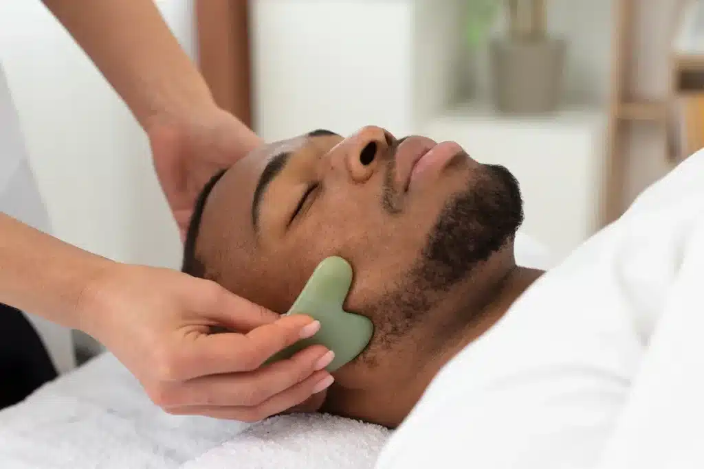 Terapeuta realizando massagem facial relaxante com pedra Gua Sha em um homem