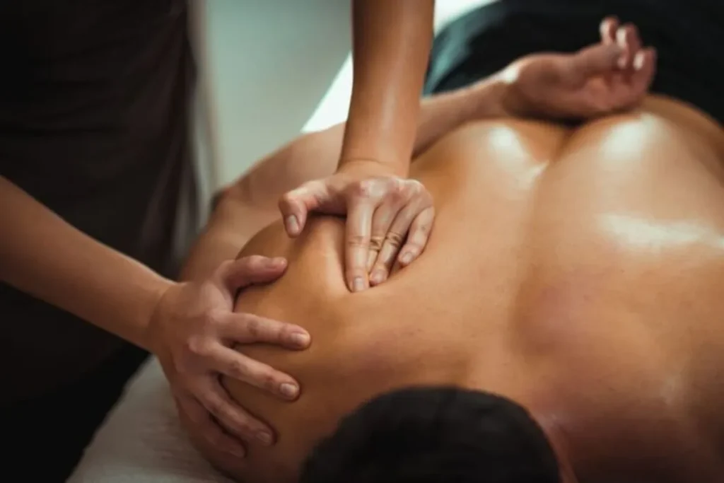 Massagista aplica uma massagem terapêutica profunda nas costas de um cliente, ilustrando a prática da massoterapia.