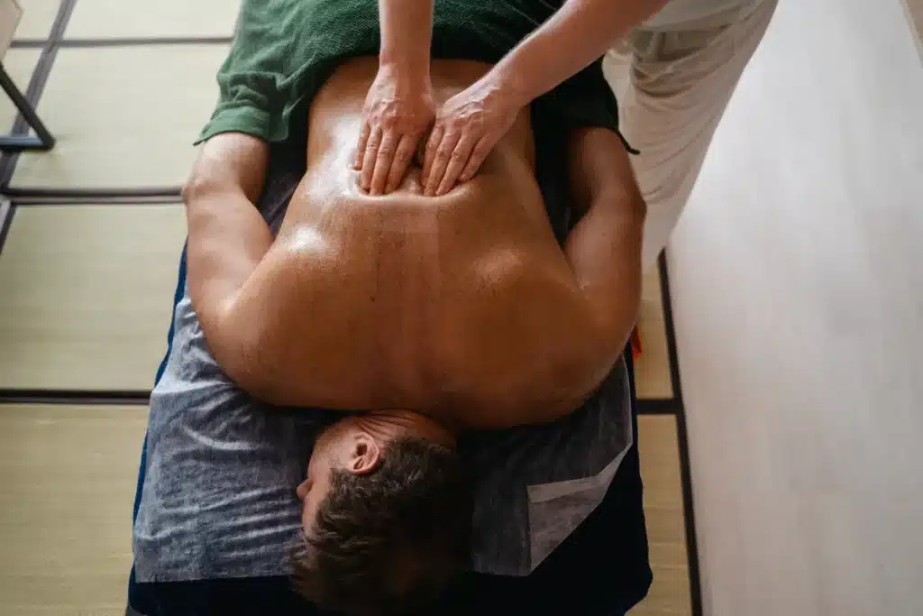 Homem deitado de bruços recebendo massagem com óleo em ambiente tranquilo, representando o atendimento em uma casa de massagem tântrica.
