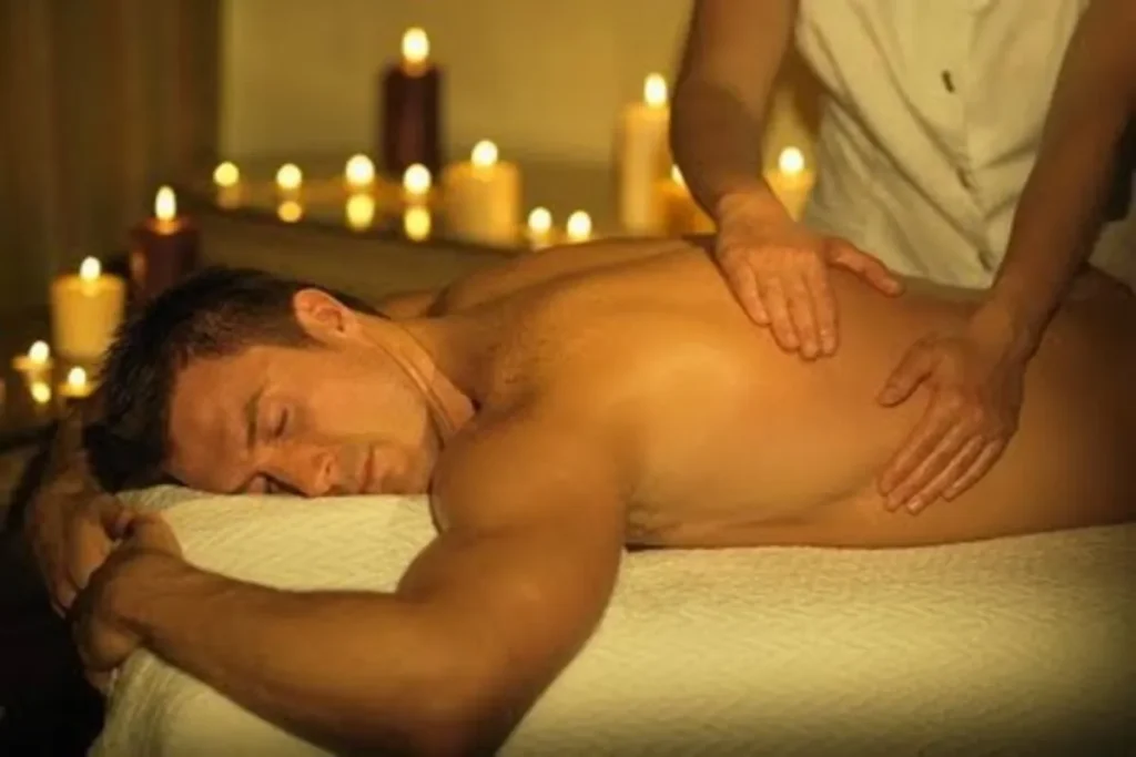Close-up de um homem recebendo massagem nas costas em uma casa de massagem ou spa. O ambiente é escuro, iluminado por velas acesas, criando uma atmosfera acolhedora e terapêutica para alívio de tensões e relaxamento.