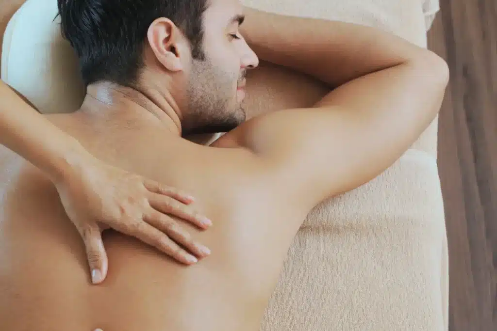 Homem recebendo uma massagem relaxante nas costas enquanto deita em uma maca confortável, com expressão serena e ambiente aconchegante.