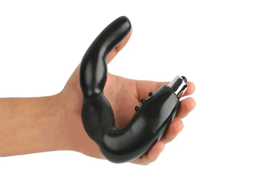 Mão segurando um massageador de próstata preto e curvo, projetado para estimulação interna. O dispositivo tem pontas texturizadas para massagem prostática, promovendo saúde pélvica e estimulação sexual.
