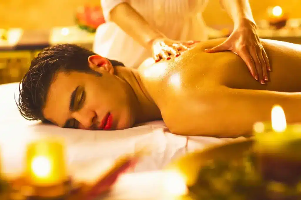 Homem recebendo massagem relaxante nas costas em ambiente com velas e iluminação suave