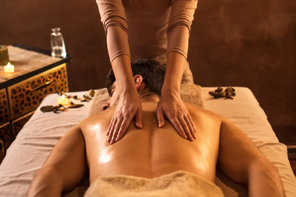 Pessoa recebendo massagem nas costas com óleo em ambiente com iluminação quente, velas acesas e clima de spa, promovendo relaxamento e bem-estar físico.