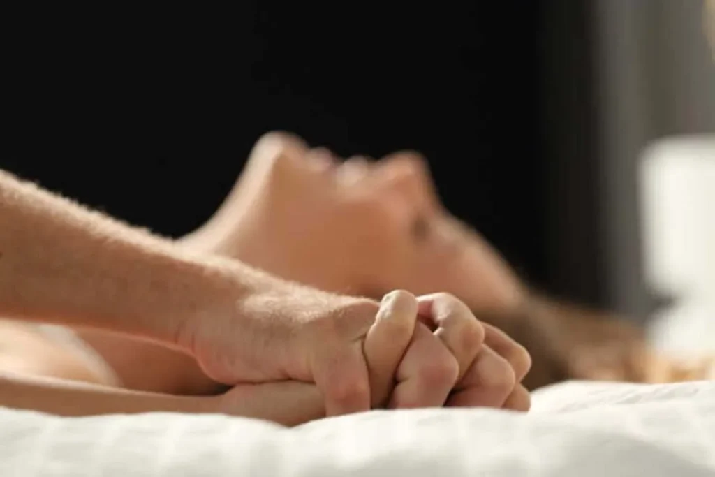 Casal de mãos dadas durante momento de prazer íntimo, representando carinho, desejo e conexão sexual.