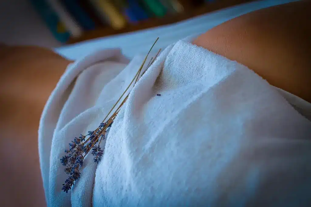 Ramos de lavanda sobre uma toalha branca cobrindo o corpo de uma pessoa, sugerindo relaxamento e bem-estar em uma sessão de massagem.