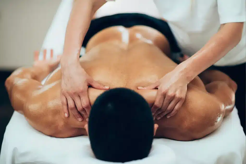 Vista aérea de um cliente deitado de bruços sobre maca, recebendo massagem nas costas com óleo aplicado pelas mãos de um terapeuta