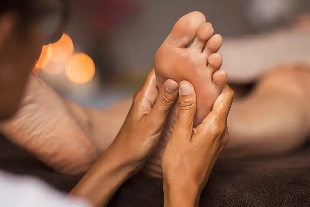 Mãos profissionais fazendo massagem na sola de um pé, com ambiente aconchegante e luz suave ao fundo