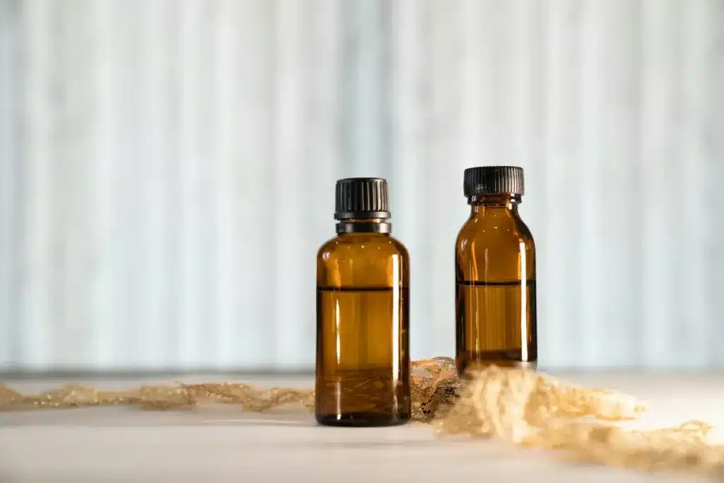 Duas pequenas garrafas de vidro âmbar com líquidos, possivelmente óleos essenciais, sobre uma superfície clara com um tecido dourado, simbolizando produtos para restaurar a energia vital.