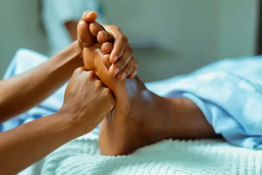Close-up de mãos massageando um pé, representando a prática da reflexologia para estimular pontos de energia vital no corpo.