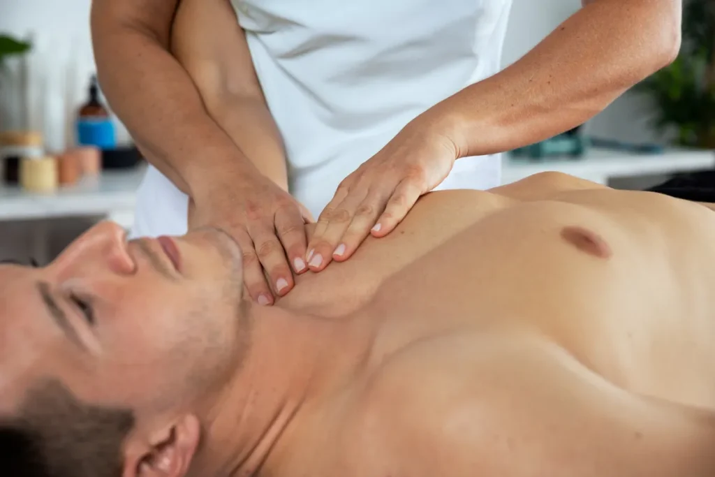 Um homem deitado em uma maca, recebendo uma massagem no pescoço e ombros de um massoterapeuta. A imagem representa uma sessão de massagem terapêutica em Indaiatuba.