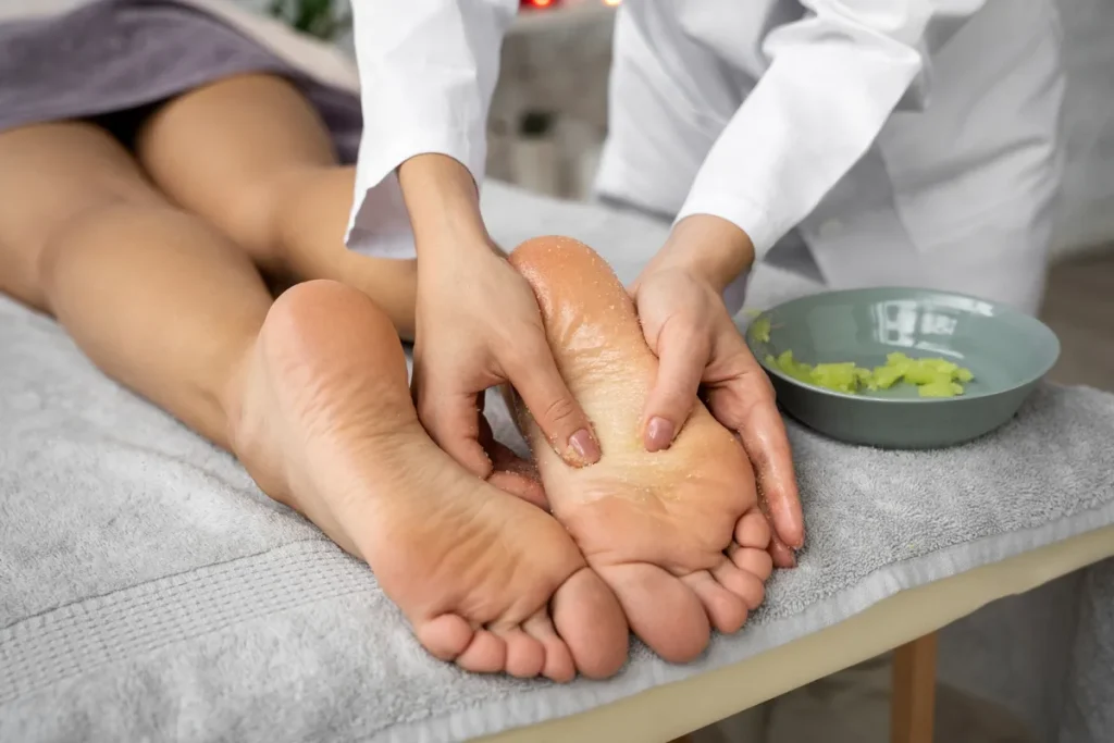 Terapeuta massageando os pés de cliente com óleo, usando as mãos, com tigela de esfoliante ao lado.