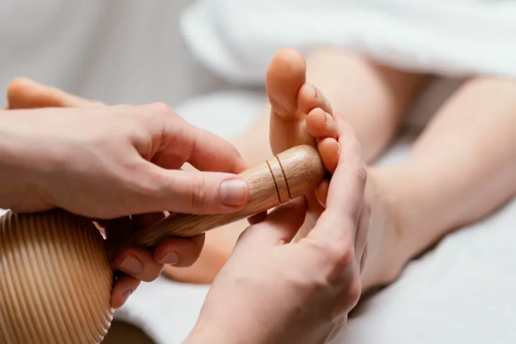 Massagem nos pés com bastão de madeira, realizada por terapeuta, com foco em relaxamento e bem-estar.