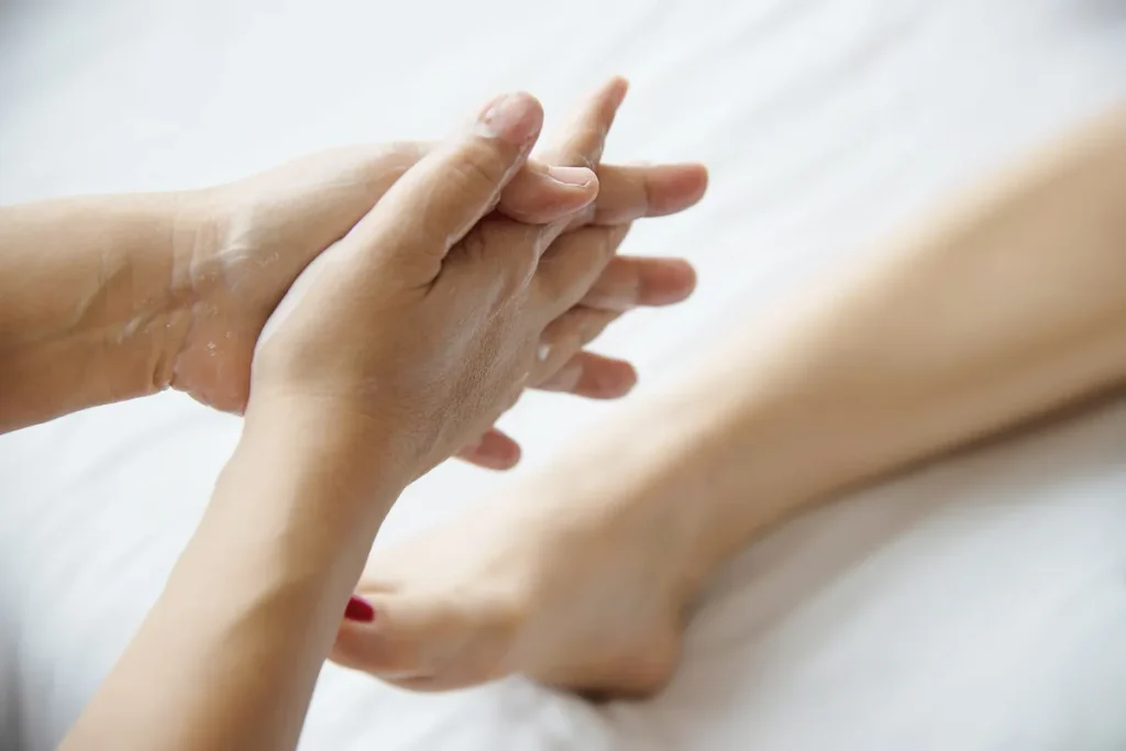 Terapeuta aquecendo as mãos com creme, preparando-se para massagem nos pés de cliente.