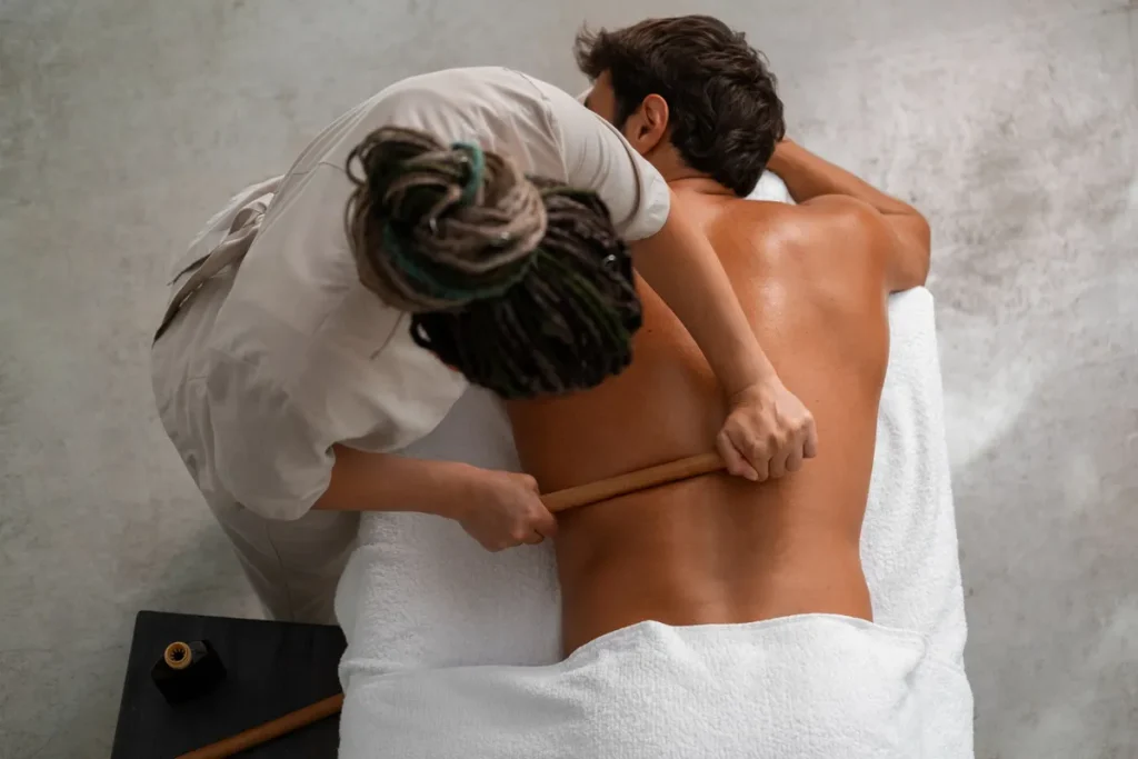 Massagista usando bastões de madeira para massagear as costas de um homem deitado em uma maca em Salvador.