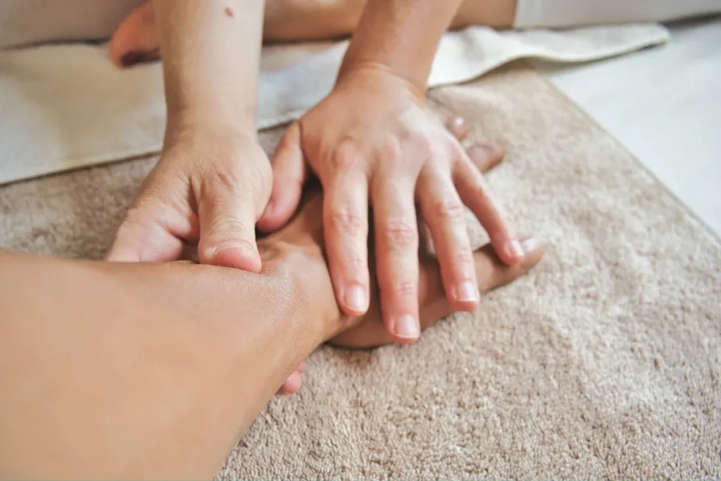 As mãos de uma pessoa massageiam a mão e o antebraço de outra, em um contexto de relaxamento e terapia. A imagem foca no toque, simbolizando bem-estar e intimidade.