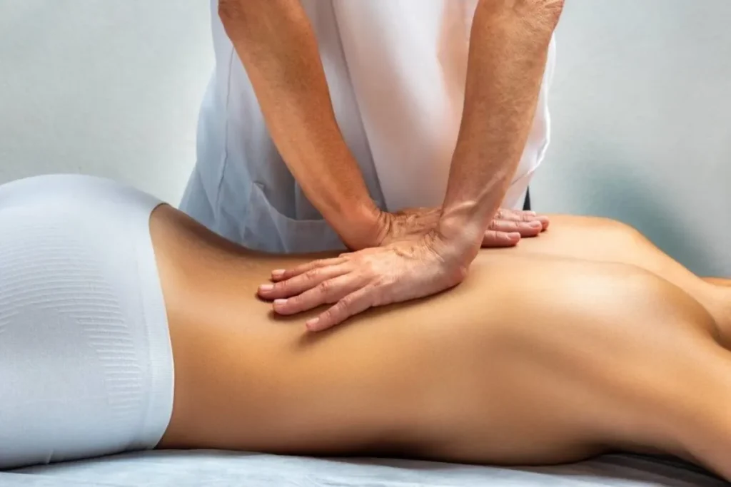 Profissional aplicando massagem nas costas de paciente para tratar dor ciática e reduzir tensão muscular.