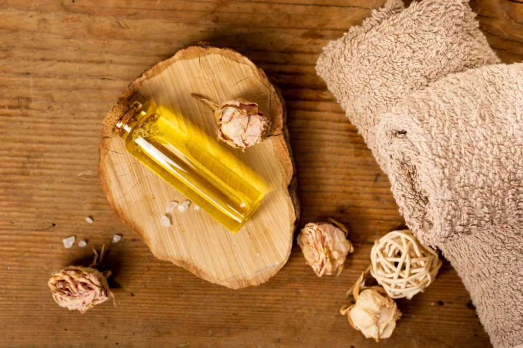 Frasco de óleo essencial natural sobre suporte de madeira, rodeado de flores secas e toalha de spa, utilizado em aromaterapia para ansiedade.