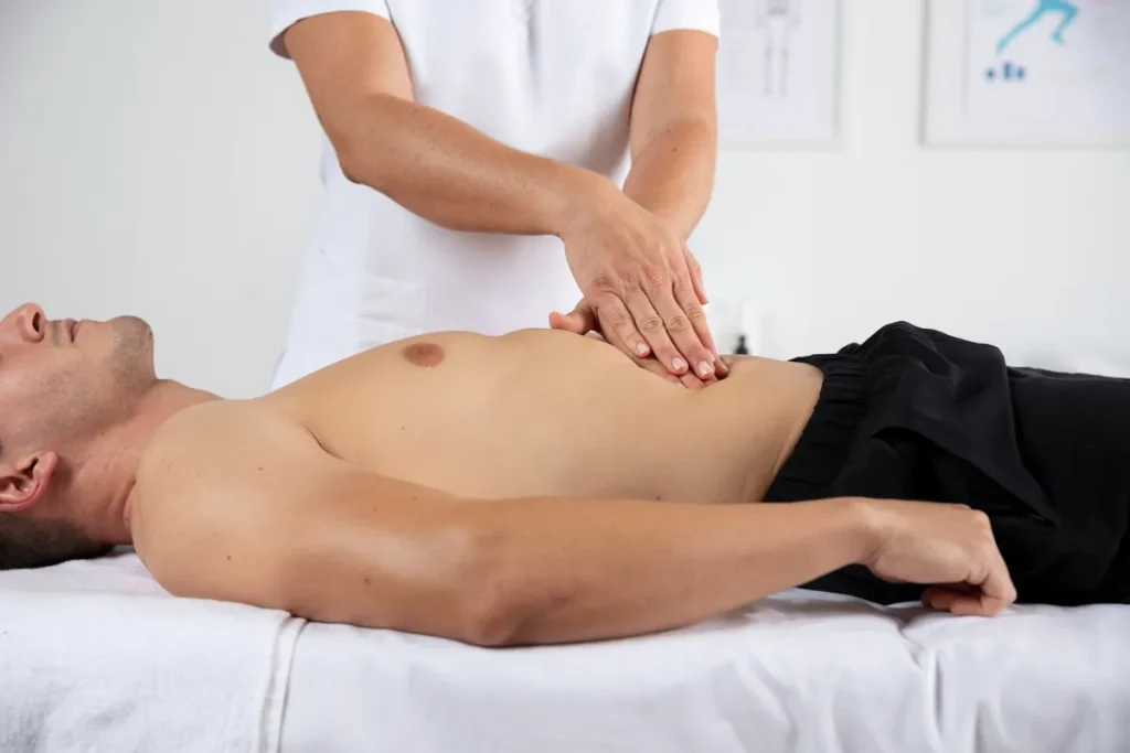 Homem recebendo massagem abdominal em clínica de terapias manuais.