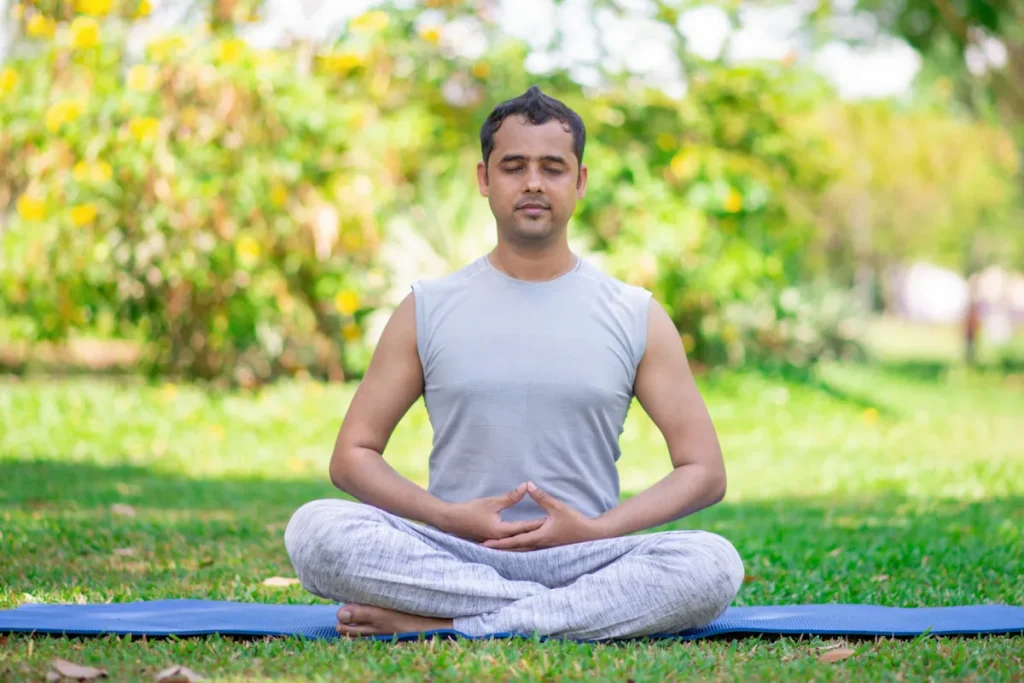 Homem praticando meditação e Tantra Yoga na postura de lótus, em um parque verde, com as mãos no jnana mudra.