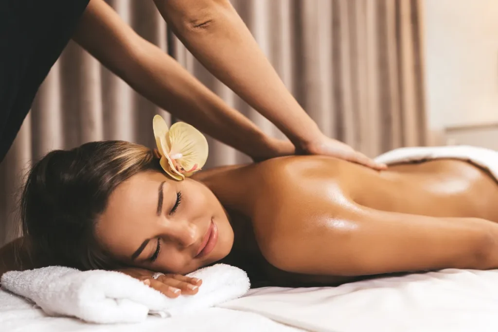 Mulher deitada em maca recebendo massagem nas costas com óleo em ambiente de spa.