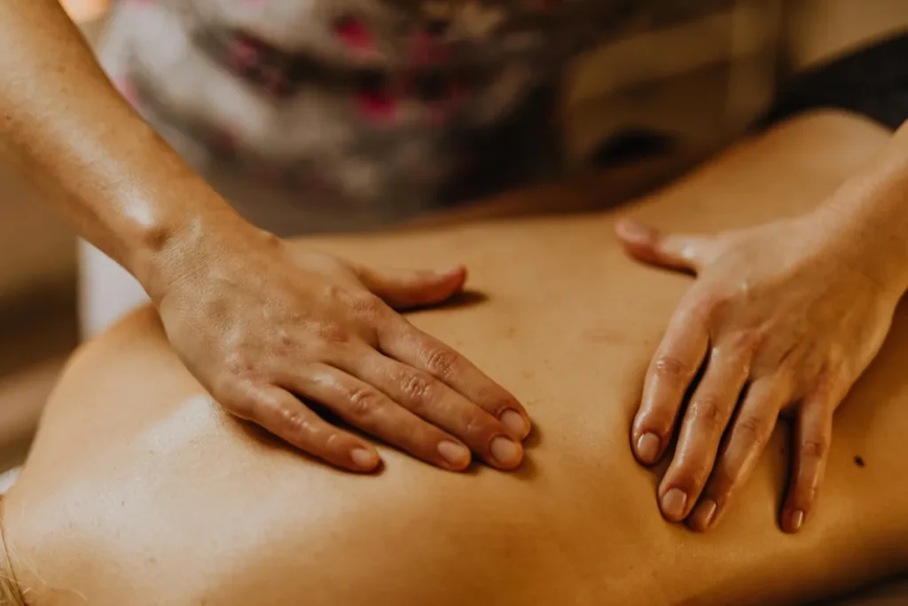 Mãos espalhando óleo e realizando massagem nas costas de uma pessoa deitada em ambiente aconchegante
