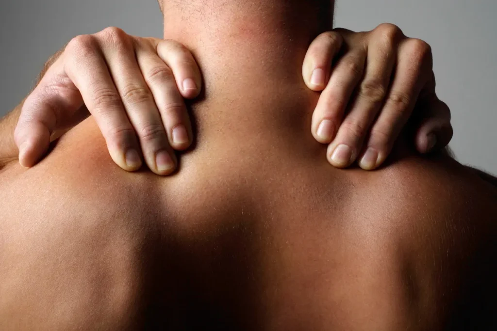 mãos pressionando a região do pescoço e ombros de um homem durante massagem