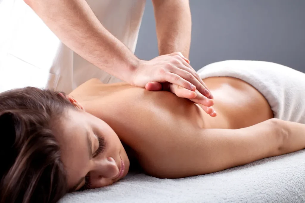 Terapeuta aplicando massagem relaxante nas costas de uma mulher deitada em maca com toalha branca.