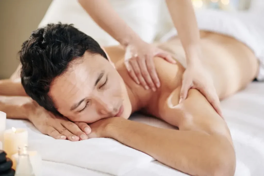 Homem recebendo massagem nas costas com óleo enquanto está deitado em maca com expressão relaxada