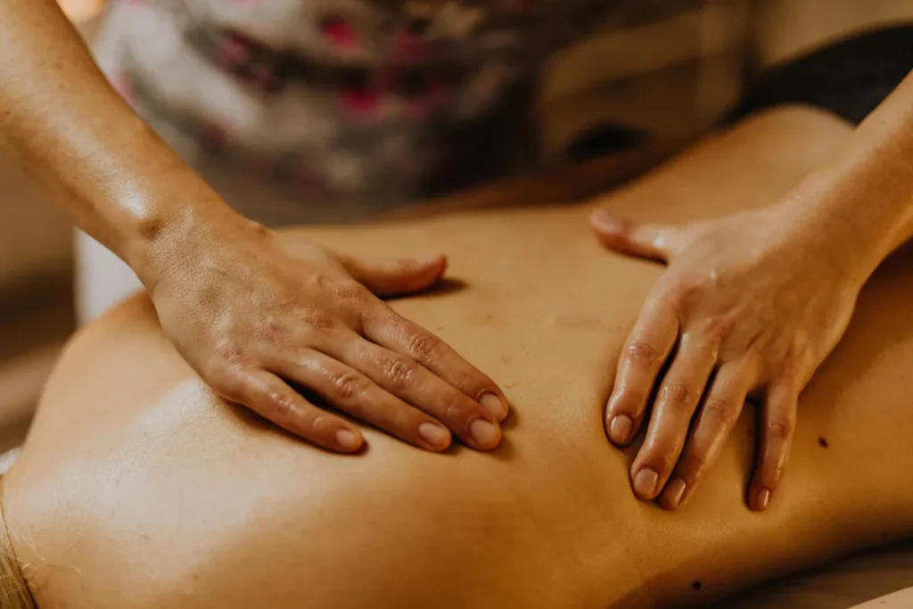 Mãos realizando movimentos suaves nas costas de cliente durante sessão de massagem com foco em relaxamento muscular