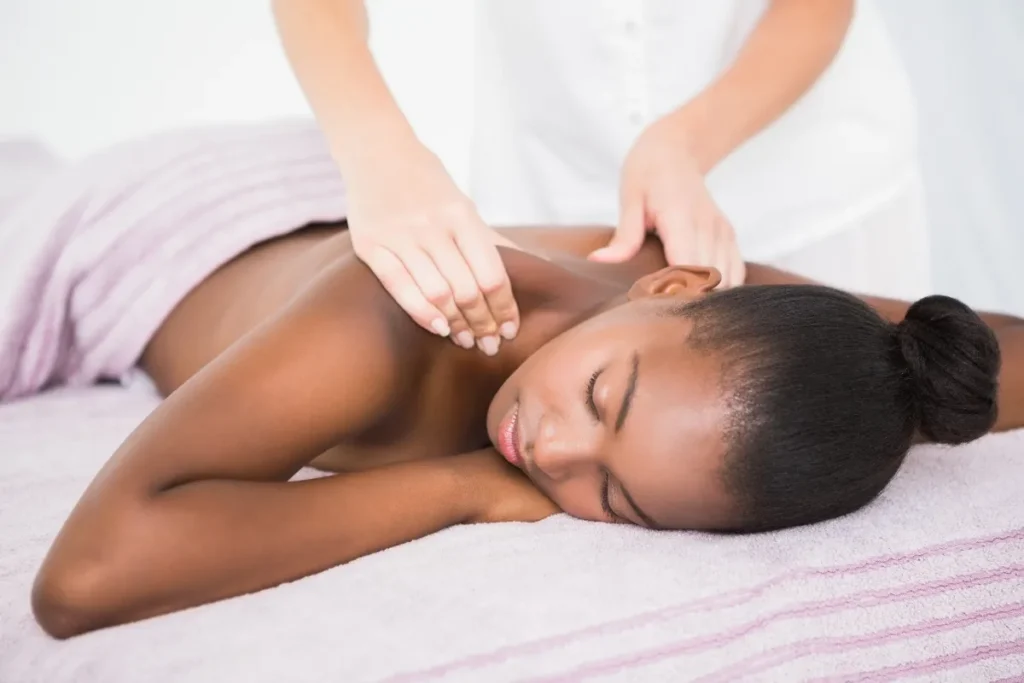 Cliente relaxando durante massagem corporal com expressão tranquila, em ambiente claro e confortável