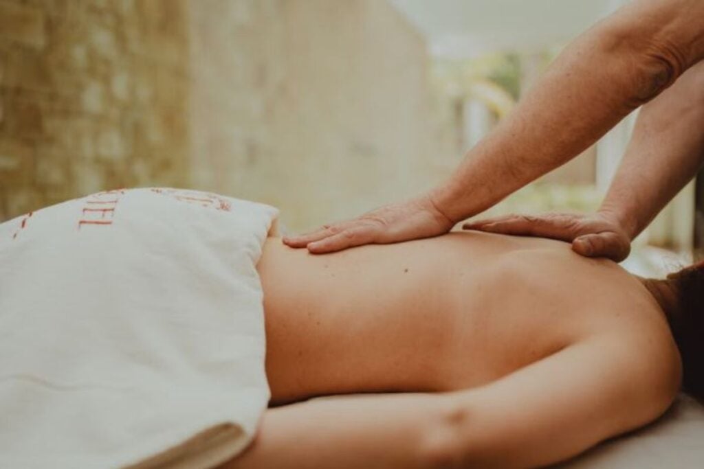 Close em uma massagem terapêutica sendo realizada nas costas de uma pessoa deitada, focando no relaxamento muscular.