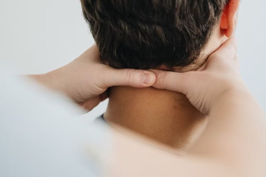 Close de mãos aplicando massagem terapêutica na região do pescoço, focando no relaxamento muscular.