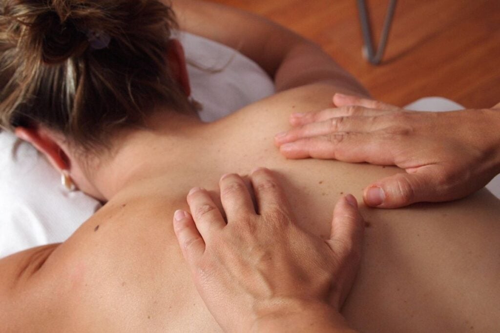 Close das mãos de um profissional aplicando uma técnica de massagem nas costas de uma pessoa deitada de bruços.