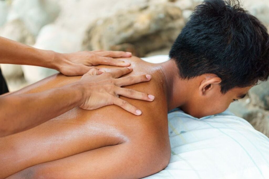 Homem deitado recebendo uma massagem relaxante nas costas e ombros, simbolizando o alívio da tensão e bem-estar físico.