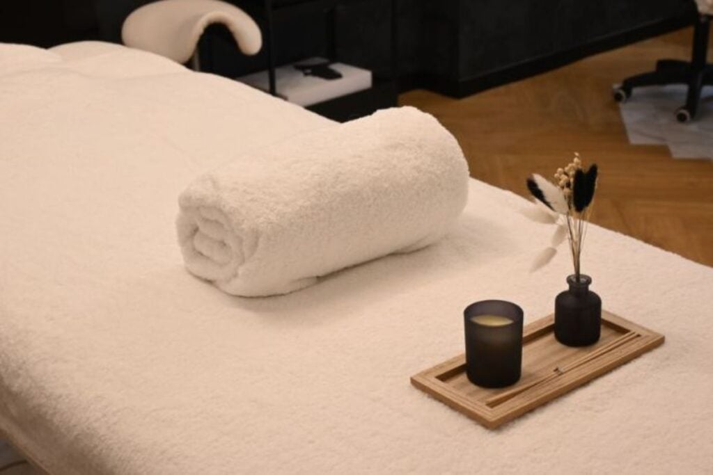 Espaço de atendimento de massagem organizado com toalha enrolada, vela e arranjo decorativo em uma maca, transmitindo acolhimento e profissionalismo.