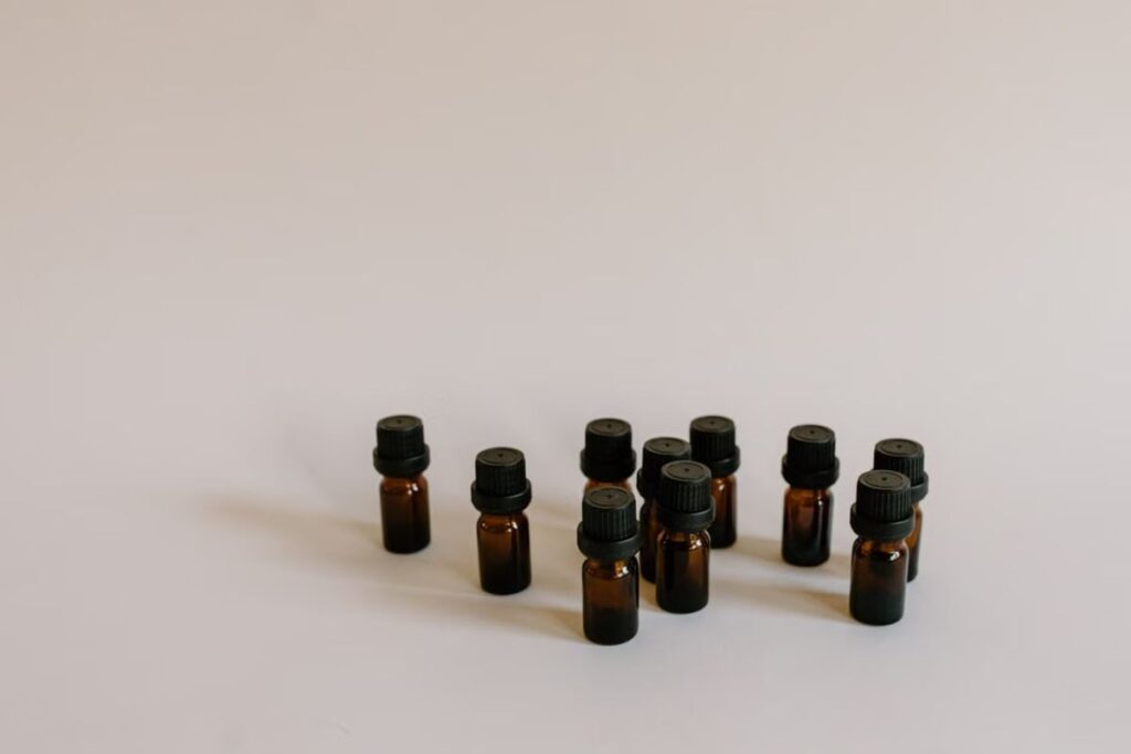 Pequenos frascos de vidro âmbar com tampas pretas dispostos sobre uma superfície clara, representando insumos de aromaterapia.