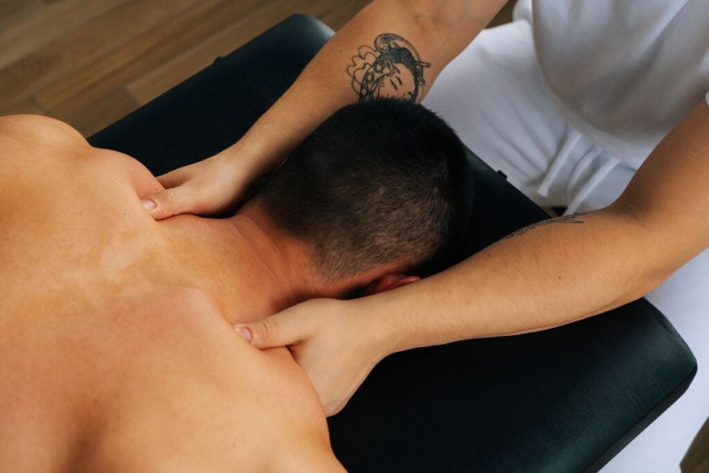 Profissional realizando massagem na região do pescoço e ombros de uma pessoa deitada.