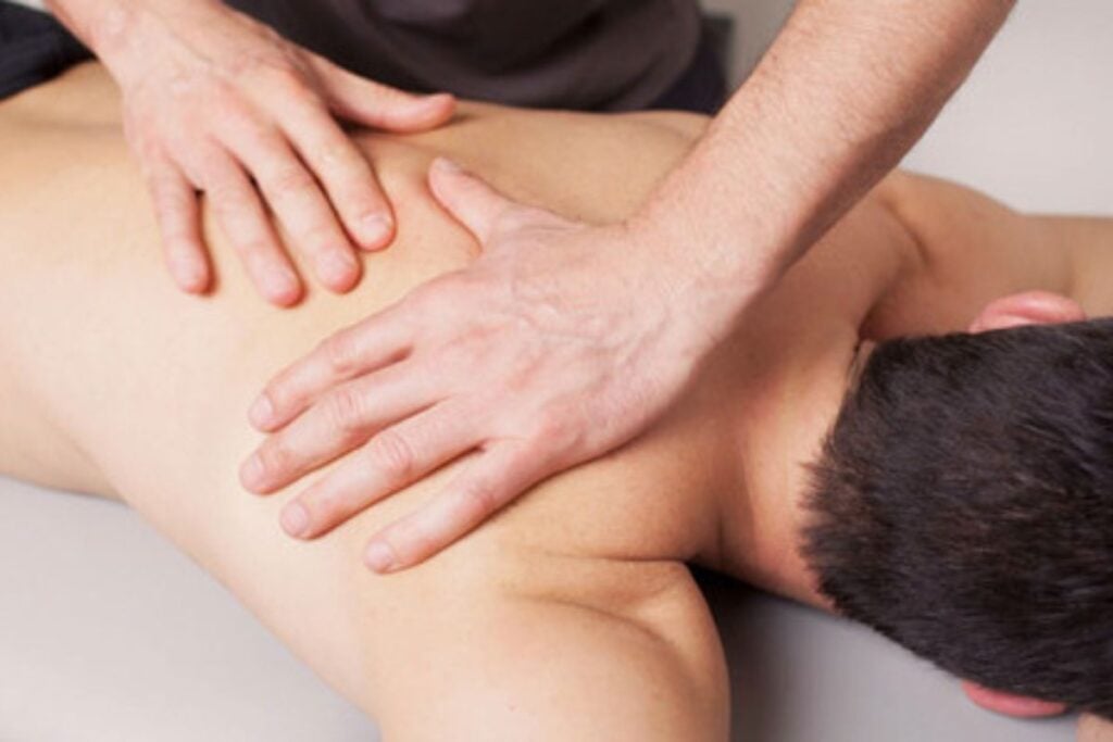 Profissional realizando massagem nas costas de uma pessoa deitada em maca.