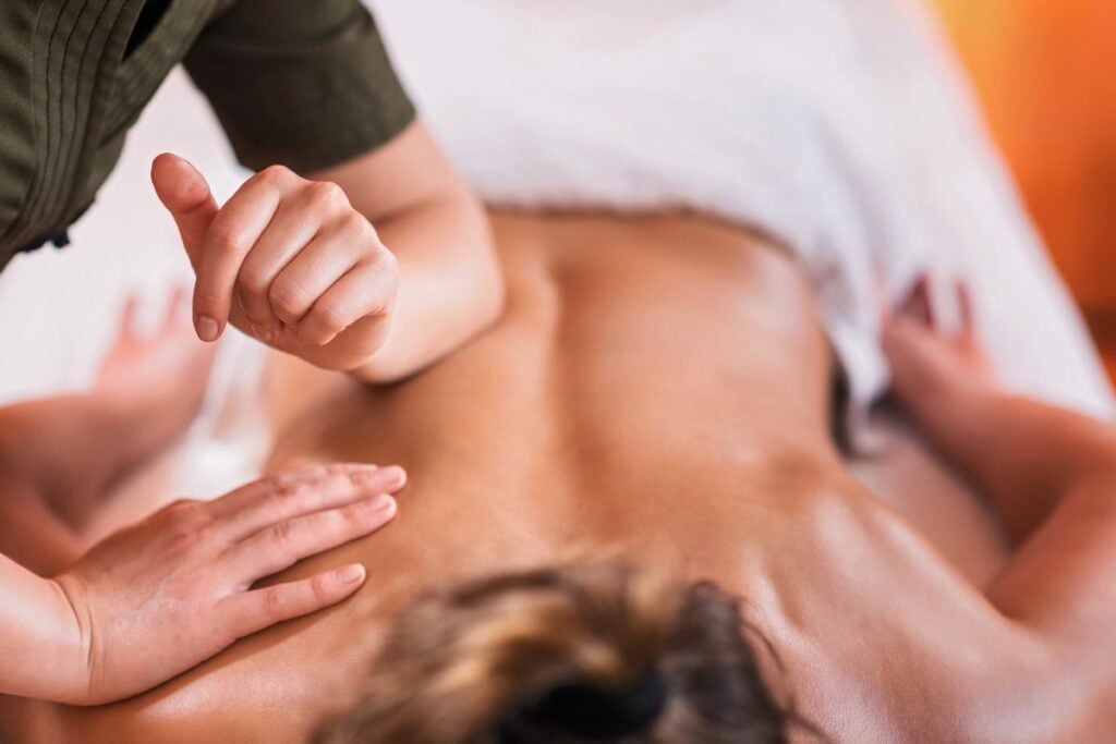 Profissional realizando massagem esportiva com pressão no pescoço e nas costas de um homem deitado.