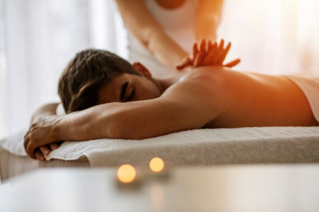 Pessoa recebendo massagem relaxante nas costas em ambiente com luz suave e velas decorativas.