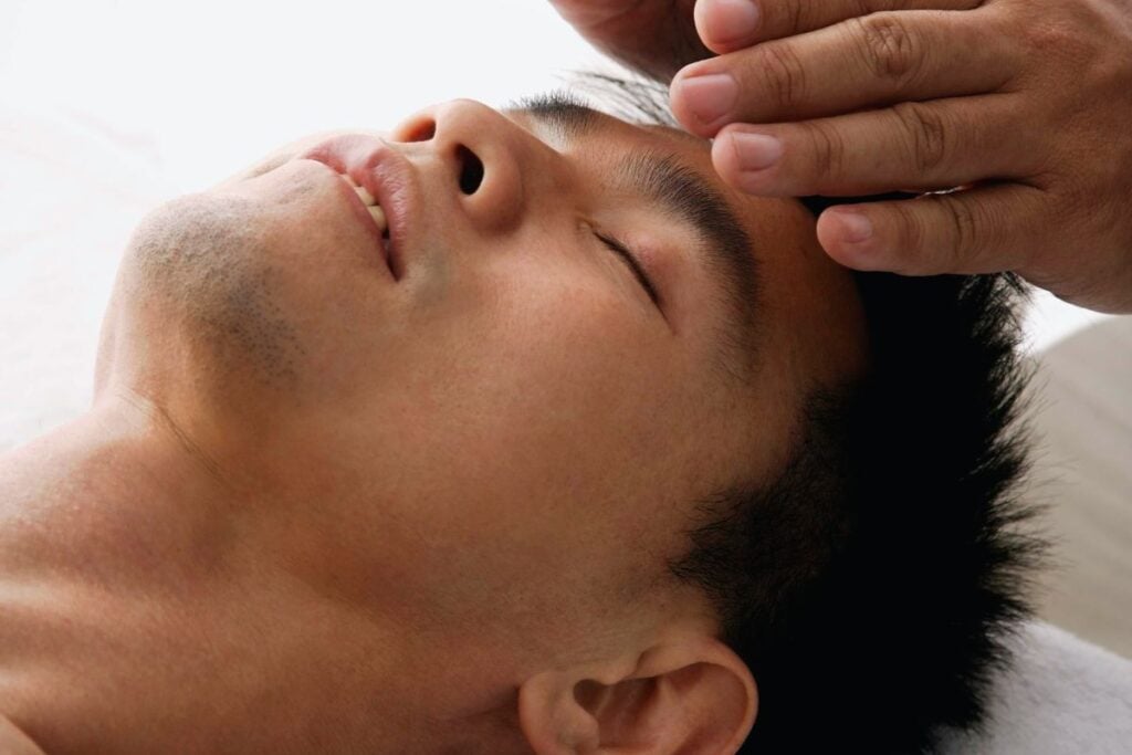 Pessoa recebendo massagem facial relaxante para aliviar tensão muscular emocional e reduzir o estresse.