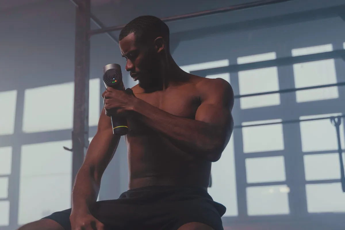 Atleta usando massageador percussivo no braço após o treino