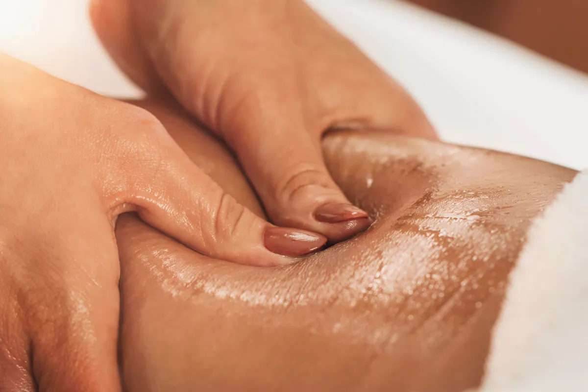 Terapeuta realizando massagem com óleo na coxa durante atendimento de bem-estar