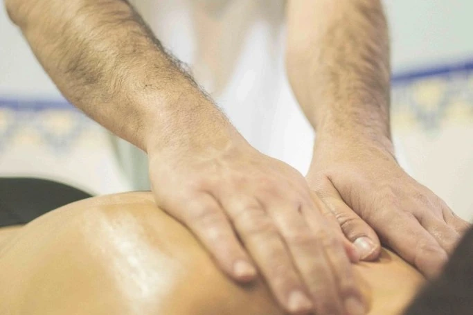 Massagista aplica massagem nas costas de um adulto em uma sala de atendimento
