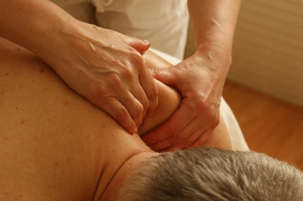 Mãos de massagista trabalham os ombros de um adulto durante uma massagem relaxante