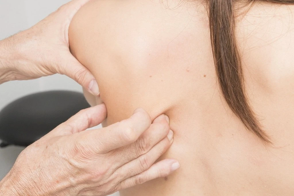 Mãos de massagista pressionam a musculatura das costas de uma mulher adulta