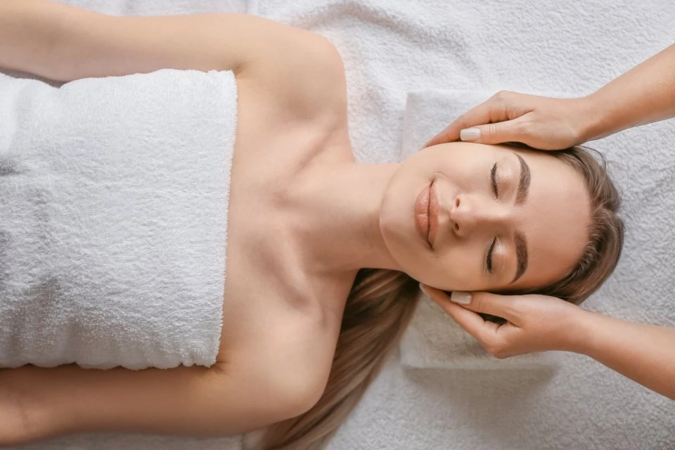 Mulher adulta recebe massagem relaxante na cabeça, deitada na maca com toalha